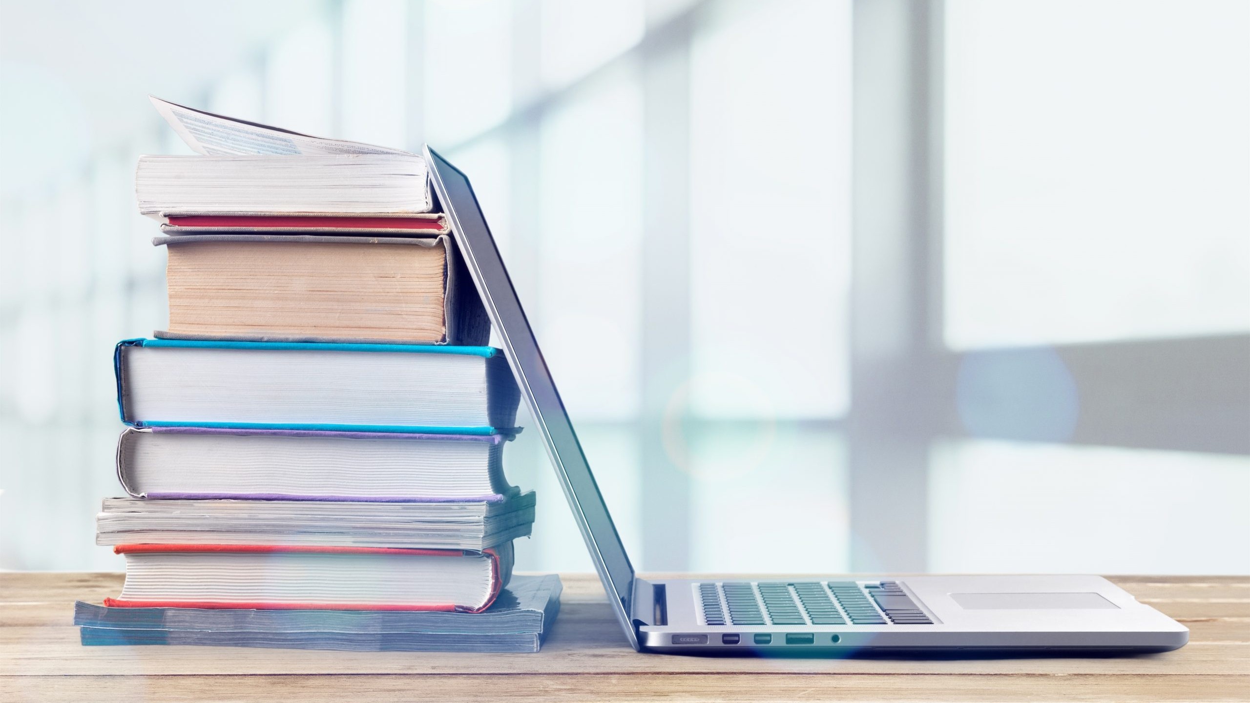 Stack of books with laptop on wooden table